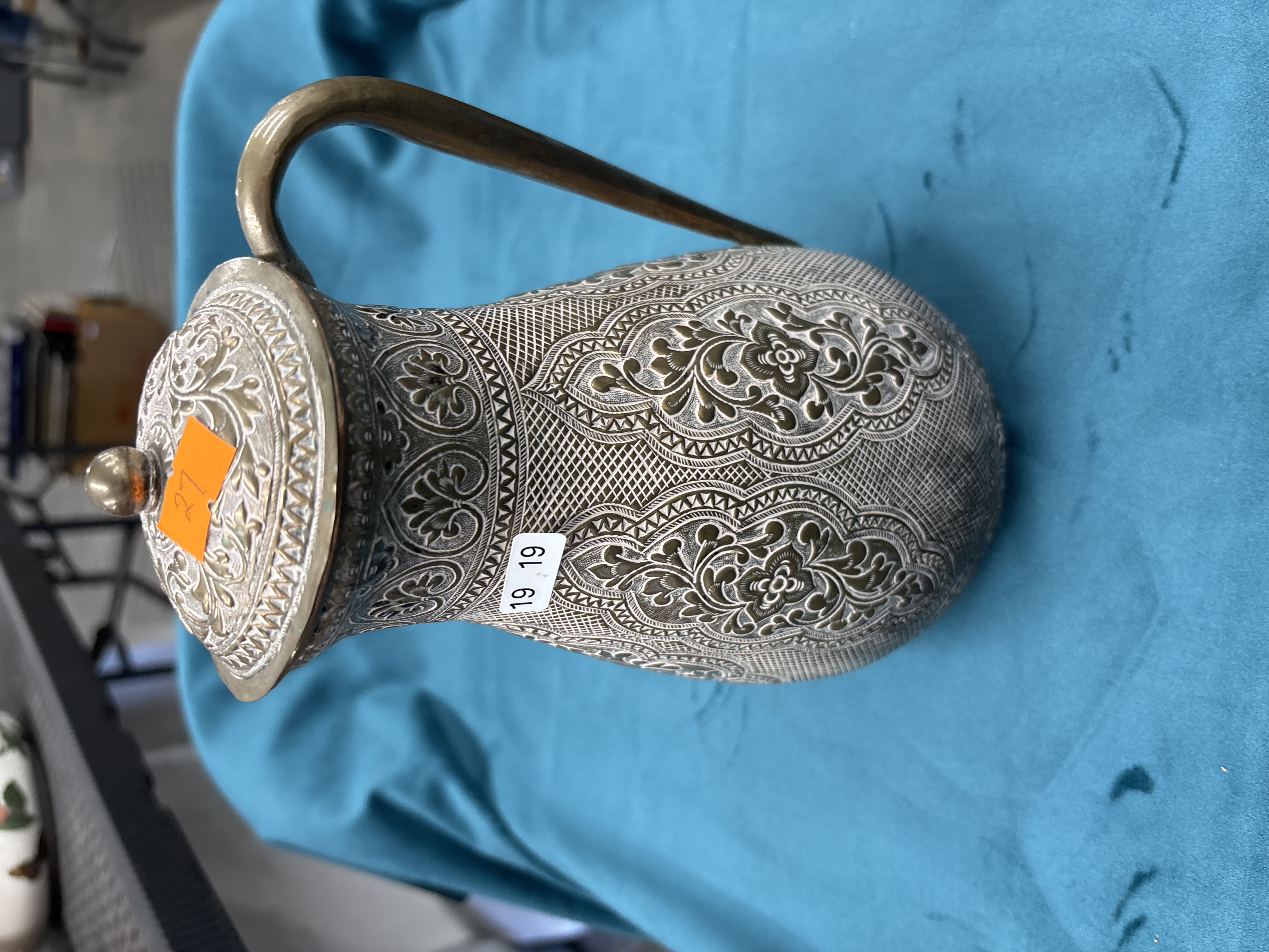 An ornate chased white metal lidded ewer with floral and foliate scrollwork