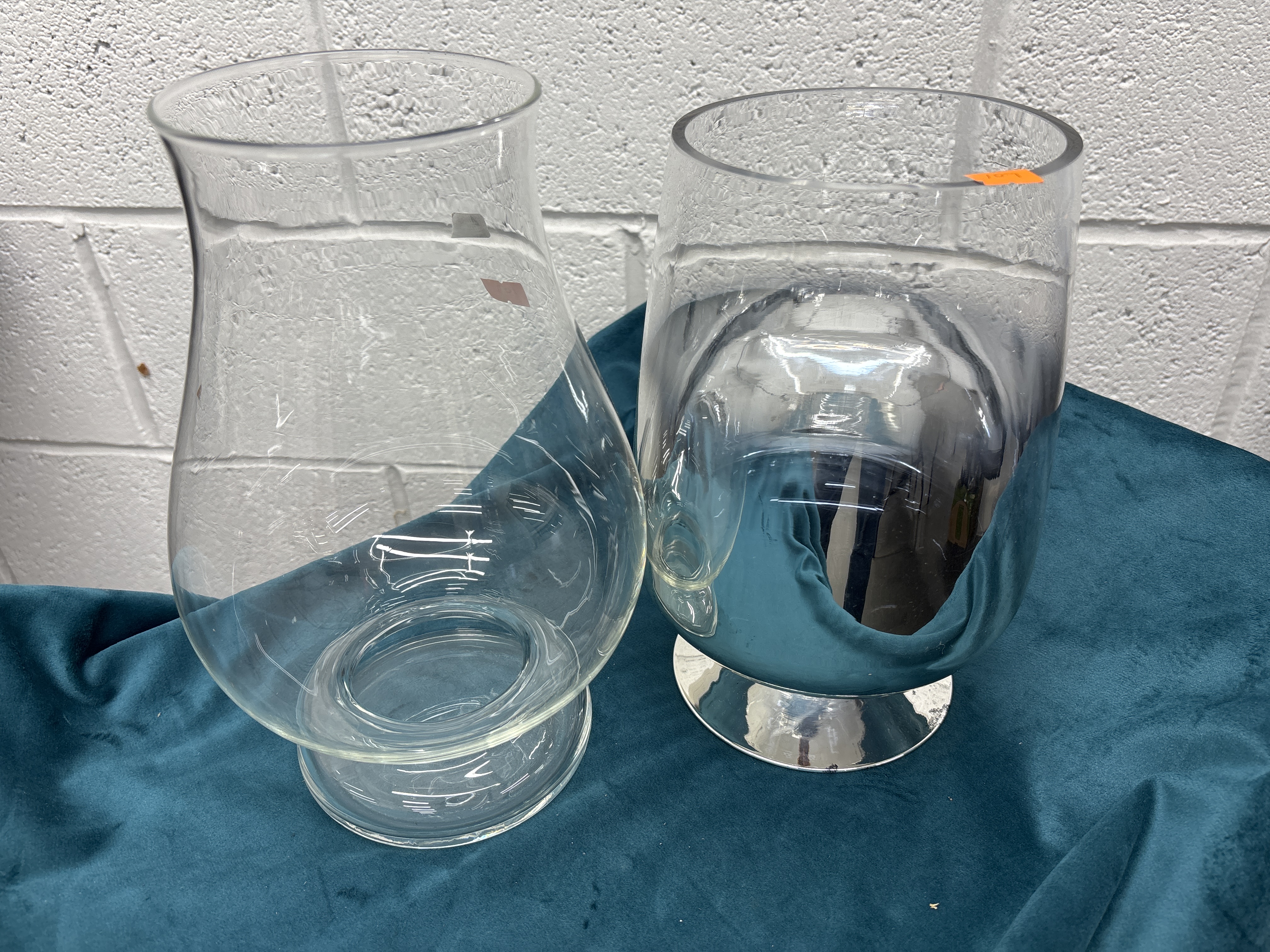 Two decorative glass vessels comprising a clear hurricane vase and a silvered glass pedestal vase