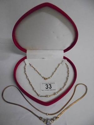 A red heart shaped box with two yellow metal necklaces.