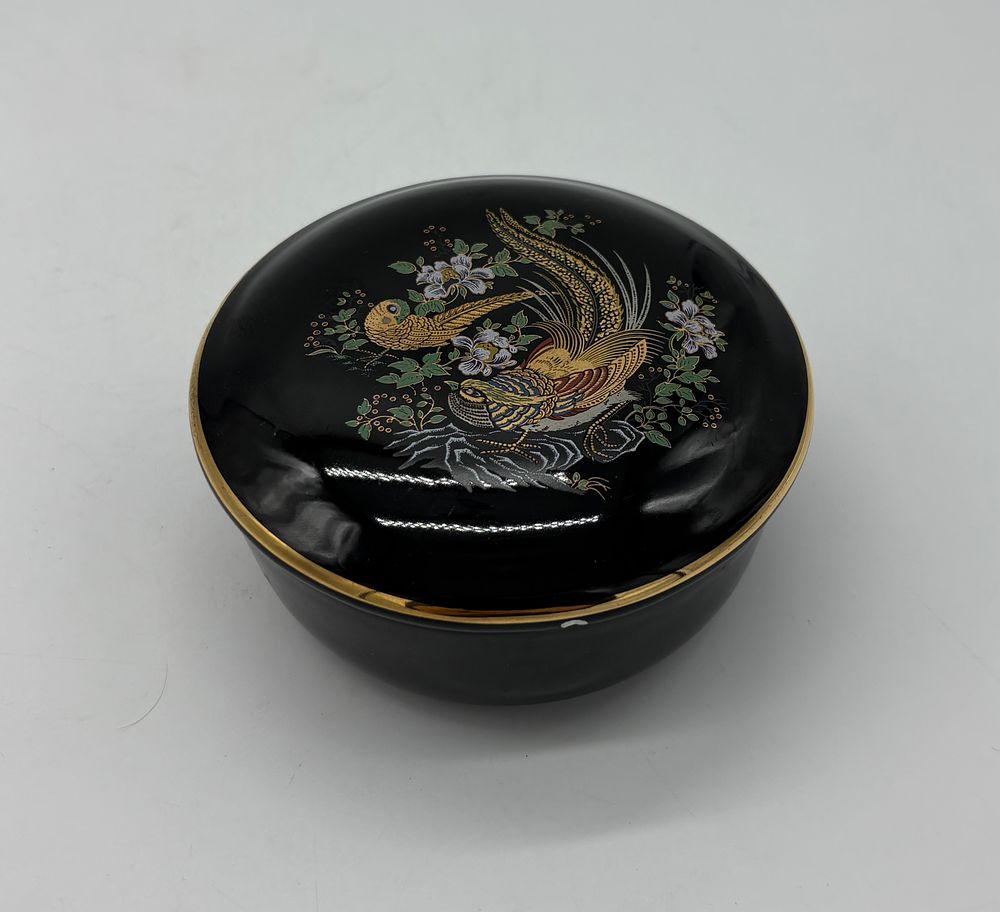 Porcelain box. Moulded and embossed porcelain box with lid. Circular black body with polychrome 