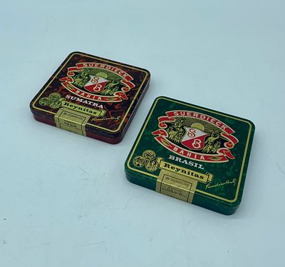 Two boxes of Suerdieck Bahia cigarettes. Metal boxes in different colours, one with a green 